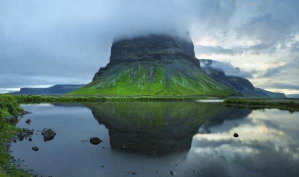 green mountain in fog with water reflection in Iceland
